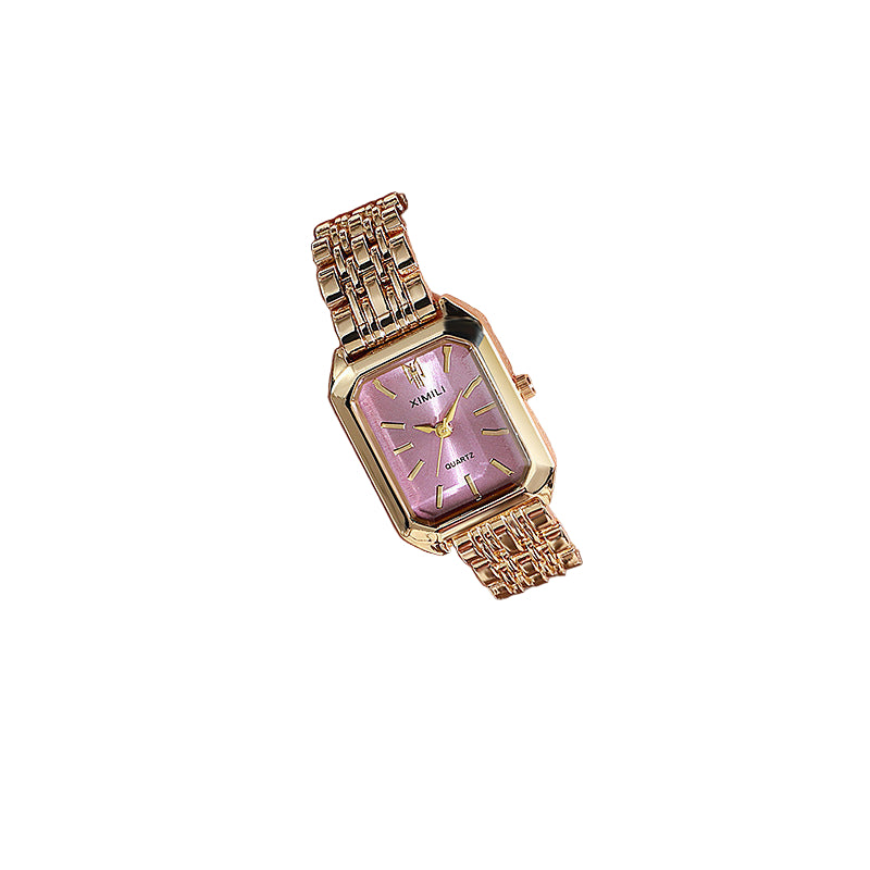 Gold wristwatch with pink face on a wrist, wearing a light-colored outfit.